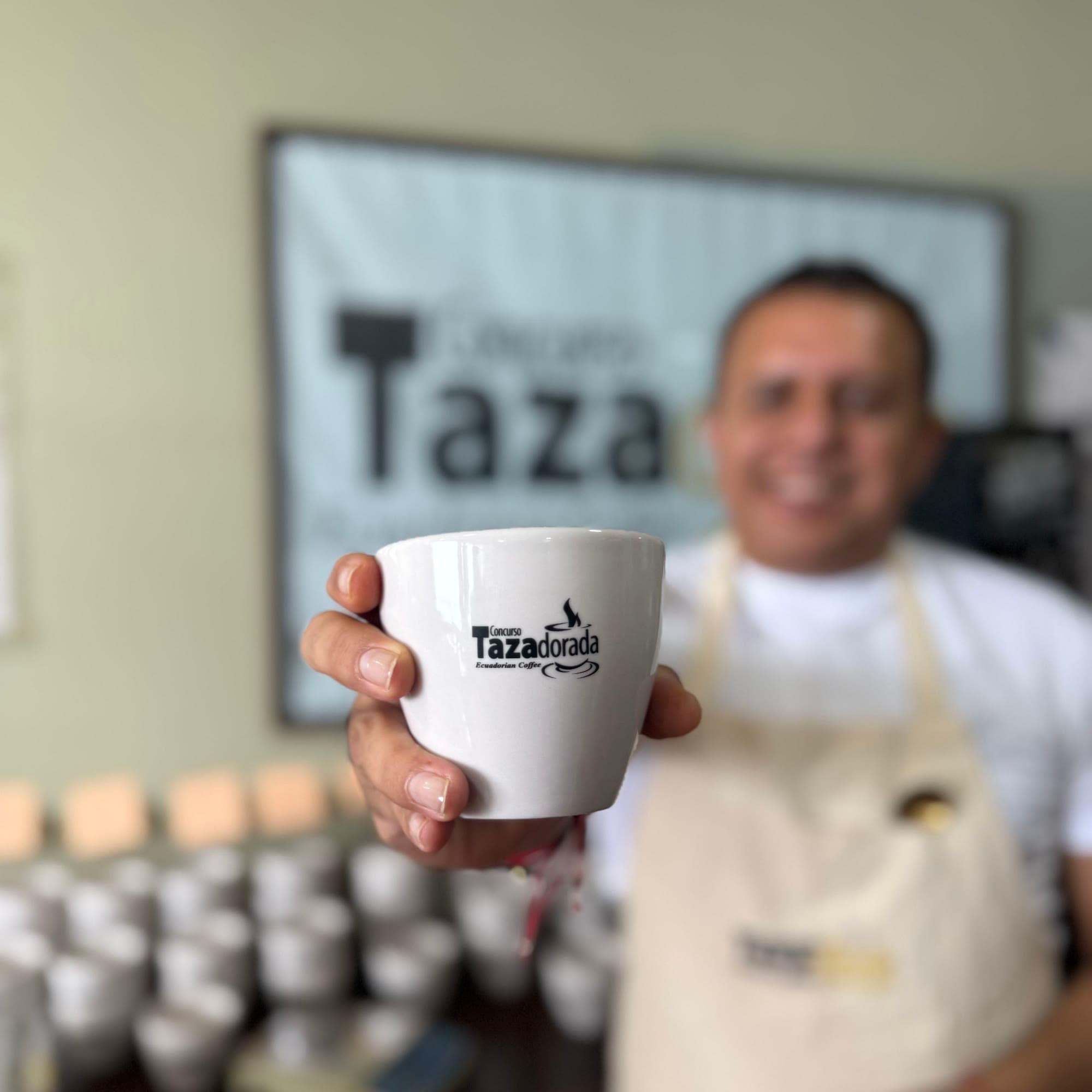 Mano sosteniendo una taza oficial del Concurso Tazadorada con su logo, en una sala de catación